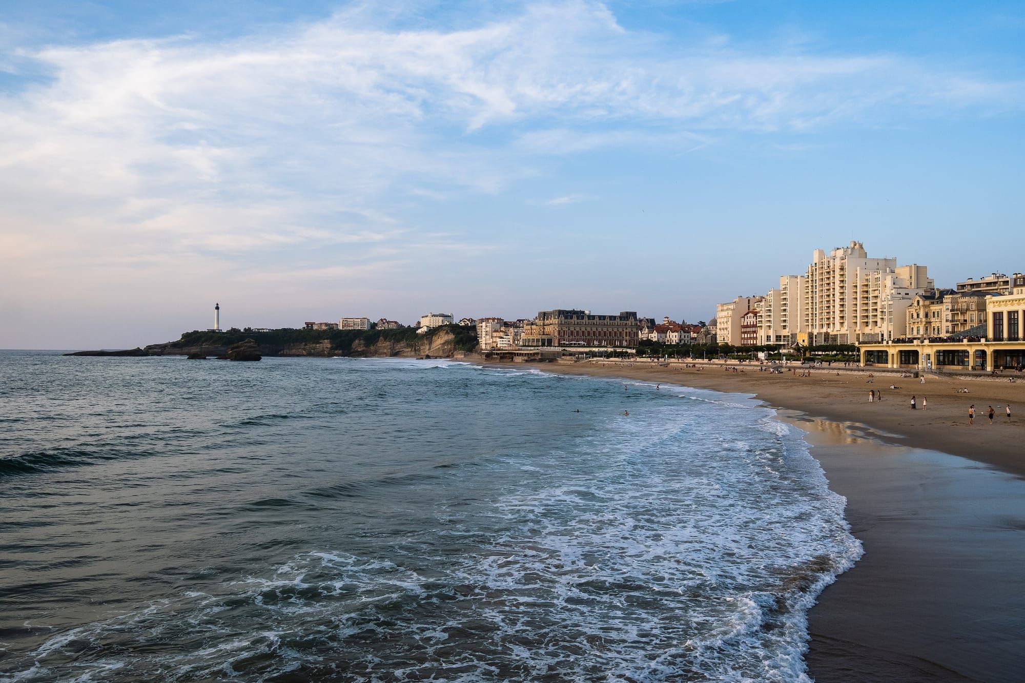 People on the Grande Plage in Biarritz, with the lighthouse along the coast